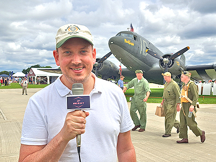 Rob Whiteley presents to camera, with a vintage plane behind, at Sywell Airshow England, UK